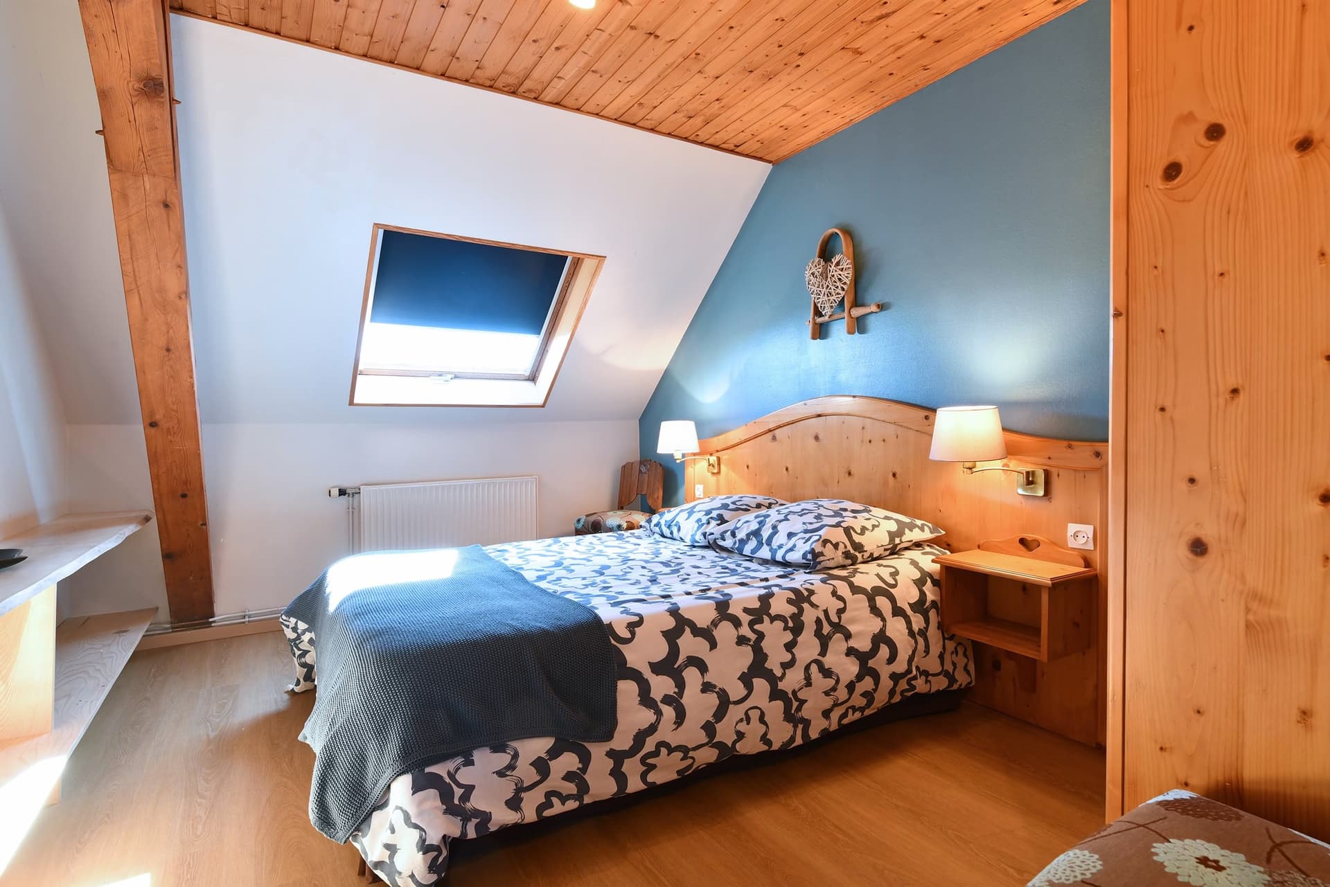 Chambre mansardée bleue, lit double, lampes de chevet allumées le soir.