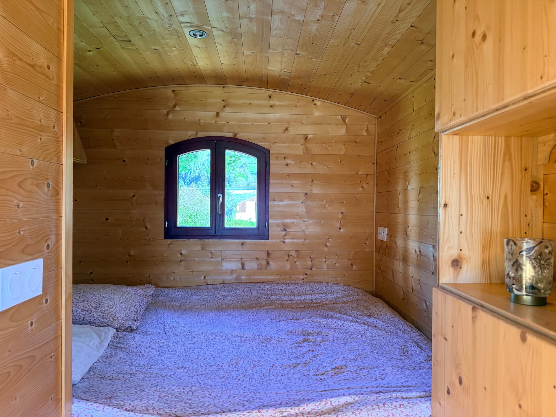 Lit en alcôve dans la roulotte, boiseries et petite fenêtre sur le jardin.